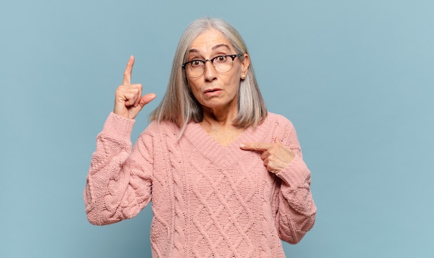 vrouw van middelbare leeftijd die trots en verrast is, zelfverzekerd naar zichzelf wijst, zich succesvol nummer één voelt