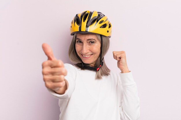 Vrouw van middelbare leeftijd die trots positief glimlacht met duimen omhoog fietshelmconcept