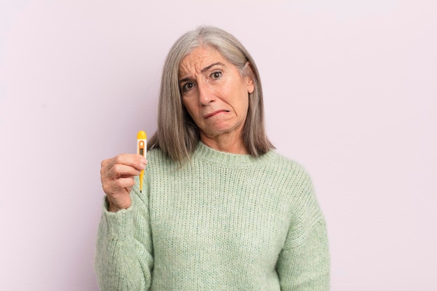 Vrouw van middelbare leeftijd die verbaasd en verward het concept van de medicijnthermometer kijkt