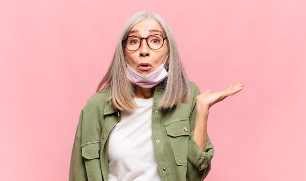 Vrouw van middelbare leeftijd die verrast en geschokt kijkt, met open mond en een object vasthoudt met een open hand aan de zijkant