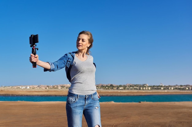 Vrouw van middelbare leeftijd die video op smartphone opneemt met buiten aan de kust