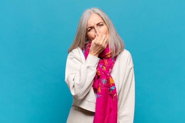 Vrouw van middelbare leeftijd die walgt en neus vasthoudt om te voorkomen dat ze een vieze en onaangename stank ruikt