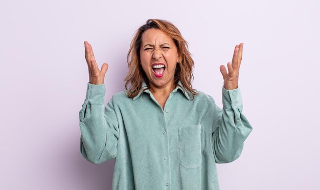 Vrouw van middelbare leeftijd die woedend schreeuwt, zich gestrest en geïrriteerd voelt met de handen in de lucht en zegt waarom ik?