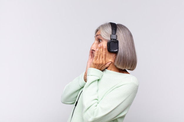 Vrouw van middelbare leeftijd die zich blij, opgewonden en verrast voelt, opzij kijkt met beide handen op het gezicht. muziek concept