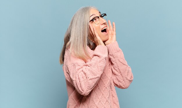 Vrouw van middelbare leeftijd die zich blij, opgewonden en verrast voelt, opzij kijkt met beide handen op het gezicht