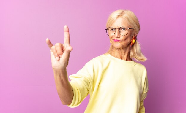 vrouw van middelbare leeftijd die zich gelukkig, leuk, zelfverzekerd, positief en rebels voelt, rock of heavy metal bord met de hand maakt