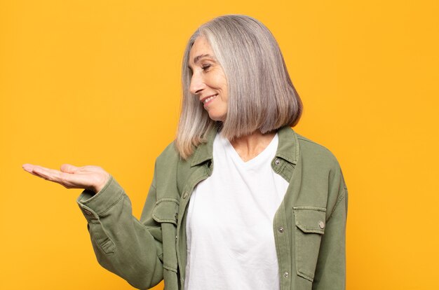 Vrouw van middelbare leeftijd die zich gelukkig voelt en terloops lacht, op zoek naar een voorwerp of concept dat aan de zijkant wordt vastgehouden