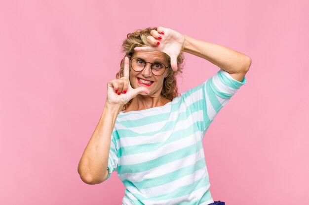 Vrouw van middelbare leeftijd die zich gelukkig, vriendelijk en positief voelt, lacht en een portret of fotolijst met handen maakt