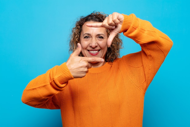 Vrouw van middelbare leeftijd die zich gelukkig, vriendelijk en positief voelt, lacht en een portret of fotolijst met handen maakt