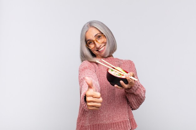 Vrouw van middelbare leeftijd die zich trots, zorgeloos, zelfverzekerd en gelukkig voelt, positief glimlacht met thumbs up aziatisch eten concept