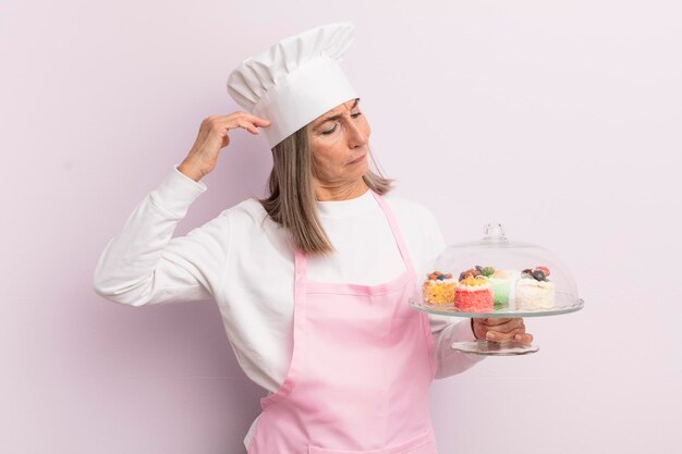 Vrouw van middelbare leeftijd die zich verbaasd en verward voelt, krabt aan het concept van bakker en gebak