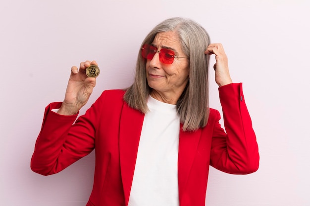 Vrouw van middelbare leeftijd die zich verbaasd en verward voelt, krabt hoofd bitcoin concept