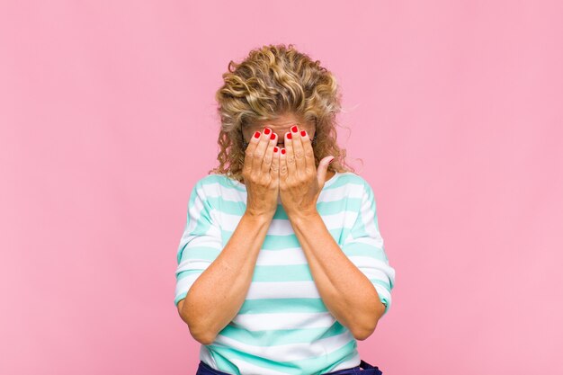 Vrouw van middelbare leeftijd die zich verdrietig, gefrustreerd, nerveus en depressief voelt, haar gezicht met beide handen bedekt, huilt