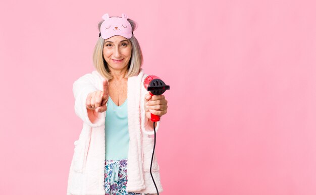 Vrouw van middelbare leeftijd, gekleed in nachtkleding met een haardroger