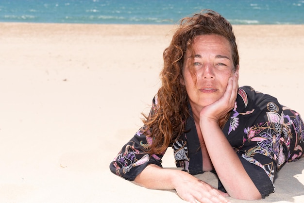 Vrouw van middelbare leeftijd geniet van vakantie aan zee, liggend op het zandstrand