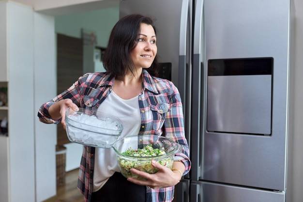 Vrouw van middelbare leeftijd in de keuken met salade en een kom ijs in de keuken