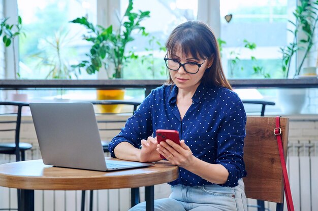 Vrouw van middelbare leeftijd in een koffieshop met een smartphone-laptop