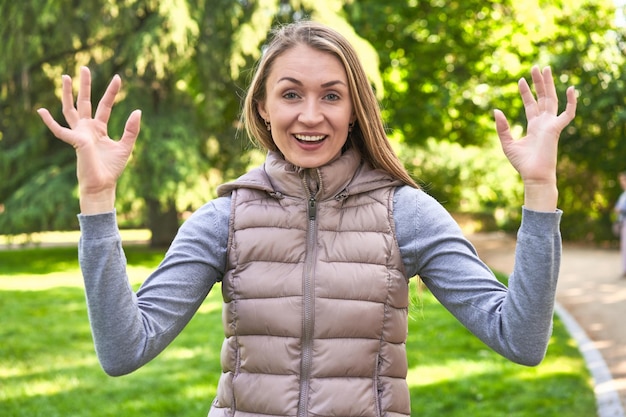 Vrouw van middelbare leeftijd in een park op een zonnige dag die een mobiele telefoongesprek met vingers toont