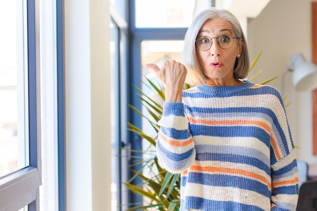 Foto vrouw van middelbare leeftijd kijkt verbaasd van ongeloof, wijst naar een voorwerp op de zijkant en zegt wow, ongelooflijk