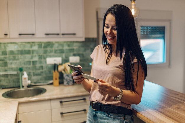 Vrouw van middelbare leeftijd met creditcard en smartphone thuis