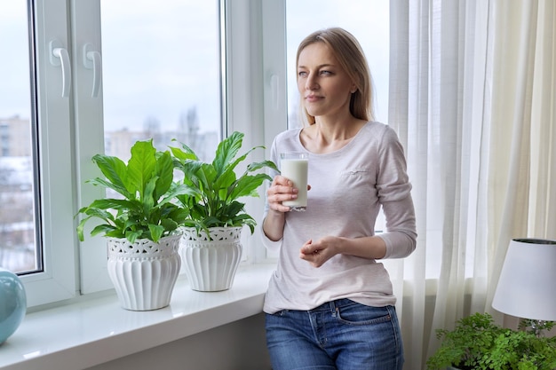 Vrouw van middelbare leeftijd met een glas melk thuis bij het raam