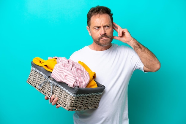 Vrouw van middelbare leeftijd met een wasmand geïsoleerd op blauwe achtergrond met twijfels en denken