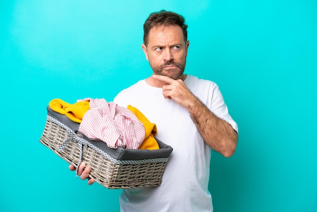 Vrouw van middelbare leeftijd met een wasmand geïsoleerd op blauwe achtergrond met twijfels en denken