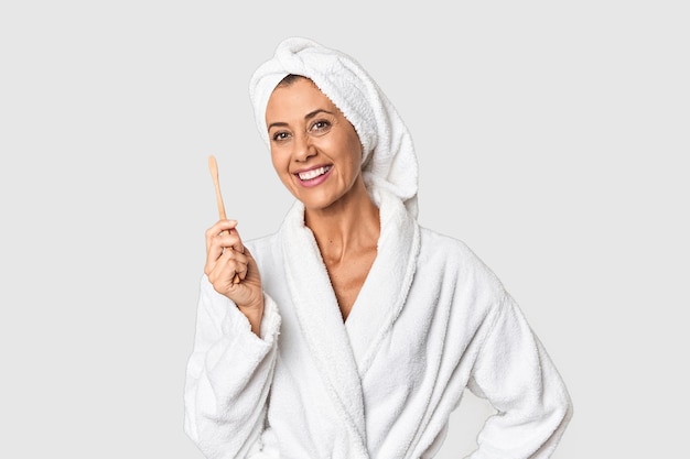 Vrouw van middelbare leeftijd met tandenborstel in badjas in studio
