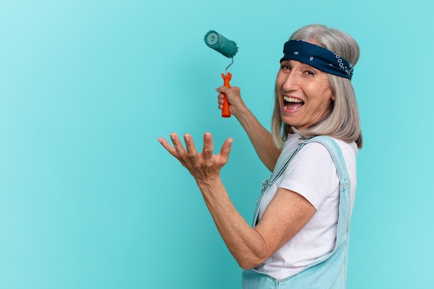 Vrouw van middelbare leeftijd met wit haar die een muur schildert