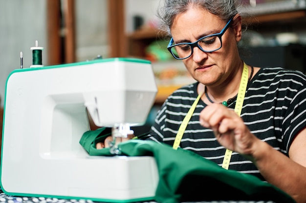 Vrouw van middelbare leeftijd met wit haar naait thuis met de naaimachine.