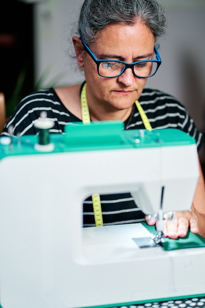 Vrouw van middelbare leeftijd met wit haar naait thuis met de naaimachine.