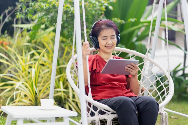 Vrouw van middelbare leeftijd ontspannen op de schommel luistert naar muziek op de tabletcomputer in de achtertuin