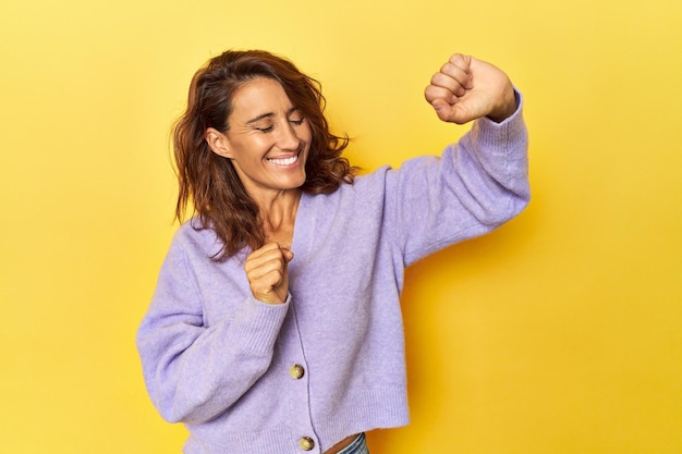 Vrouw van middelbare leeftijd op een gele achtergrond dansen en plezier maken