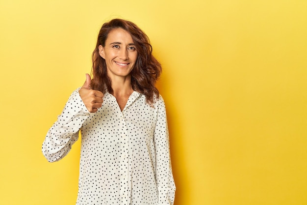 Vrouw van middelbare leeftijd op een gele achtergrond glimlachend en duim omhoog