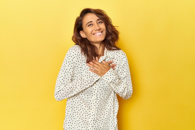 Vrouw van middelbare leeftijd op een gele achtergrond heeft een vriendelijke uitdrukking en drukt de handpalm op de borst. Liefdesconcept