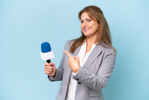 Vrouw van middelbare leeftijd tv-presentator over geïsoleerde blauwe achtergrond wijzend terug