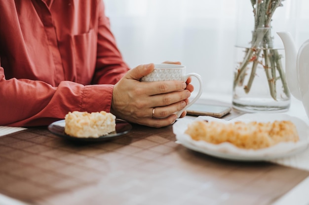 Vrouw van middelbare leeftijd zit aan de tafel in de gezellige keuken in het appartement en drinkt thee met appeltaart op gezellige herfstdagen