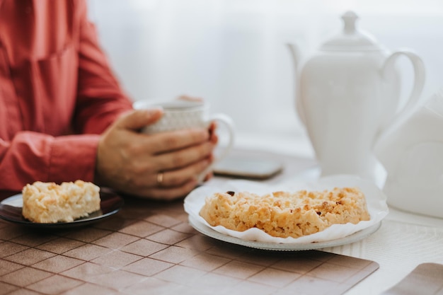 Vrouw van middelbare leeftijd zit aan de tafel in de gezellige keuken in het appartement en drinkt thee met appeltaart op gezellige herfstdagen