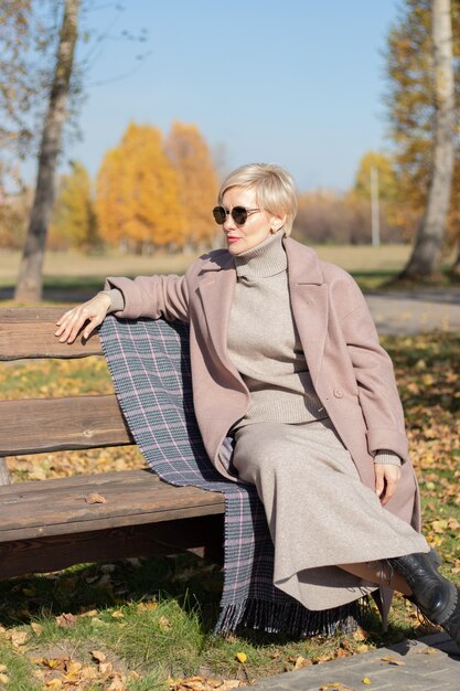 Vrouw van middelbare leeftijd zit in de herfst op een parkbank