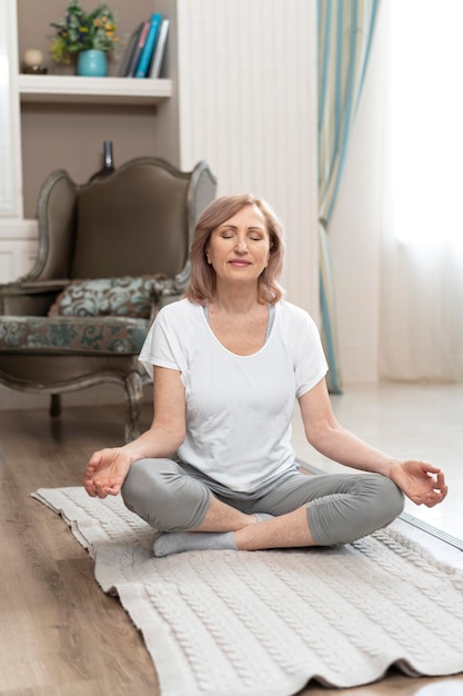 Vrouw van middelbare leeftijd zittend op de vloer op yogamat in lotushouding. Mudra-gebaar maken.