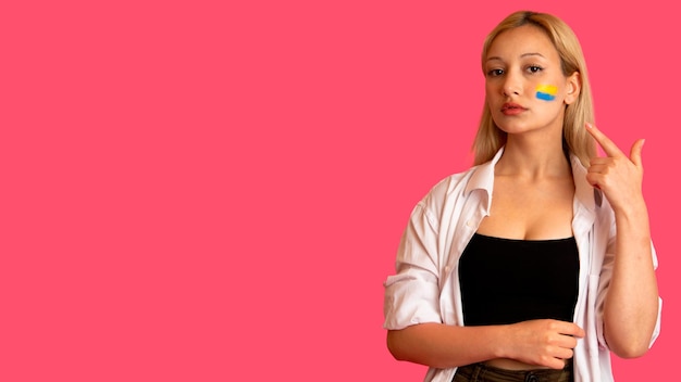 Vrouw van modeluitstraling met de vlag van Oekraïne op haar gezicht houdt poseren op een roze achtergrond