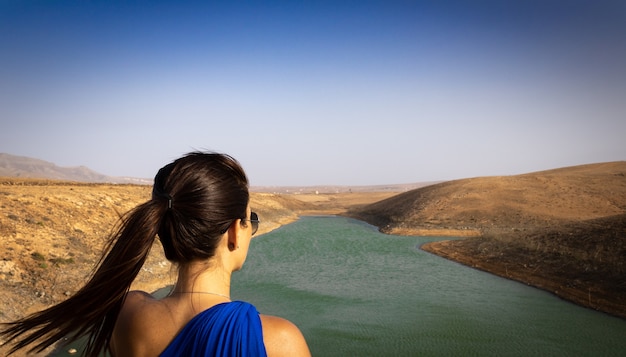 Vrouw vanaf de achterkant kijken naar het landschap van een meer met groen water.