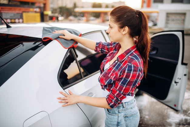 Vrouw veegt de auto af met een doek na het wassen, polijstproces op self-carwash. Dame schoonmaak voertuig