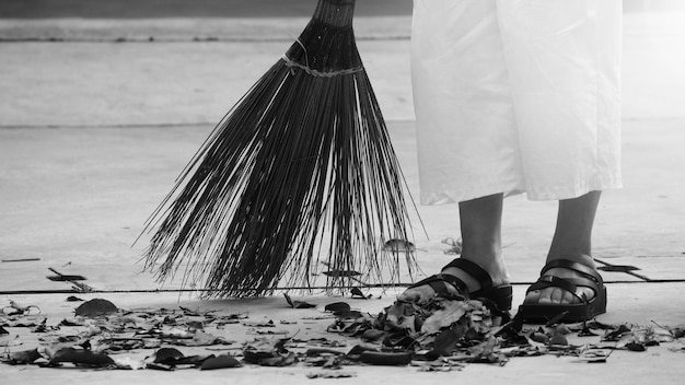 Vrouw veegt droge bladeren op de cementvloer met lange houten bezem