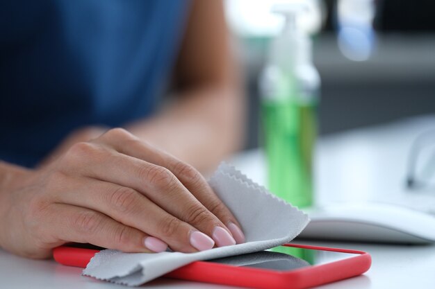 Vrouw veegt het scherm van de mobiele telefoon af met een antiseptische servetclose-up