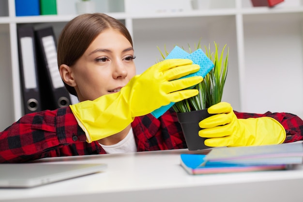 Vrouw veegt stoffige groene kamerplantbladeren binnenshuis af