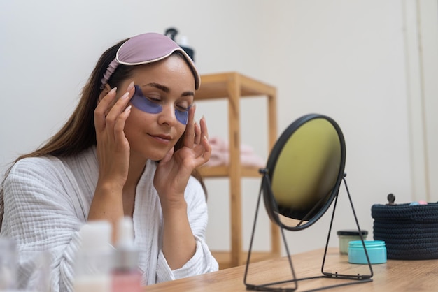 Vrouw verbetert haar anti-aging huidverzorging met ooglappen en kijkt naar de spiegel tijdens een thuis spa dag