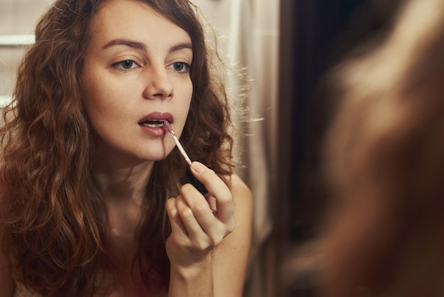 Vrouw verft haar lippen met lippenstift voor spiegel