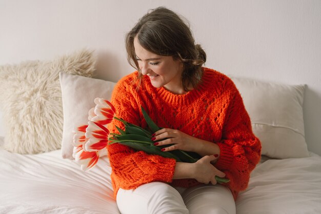 Vrouw verheugt zich over tulpen. Mooie vrouw zit thuis op het bed.