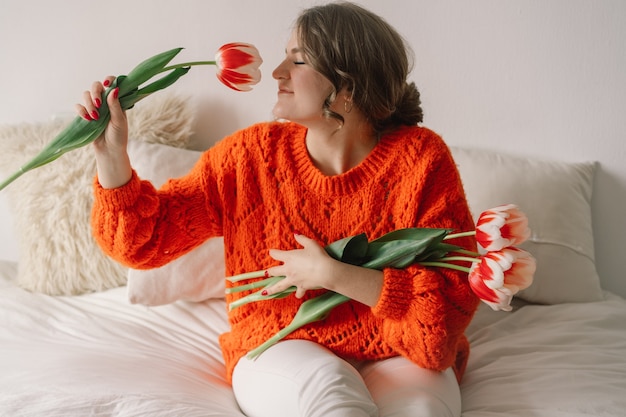 Vrouw verheugt zich over tulpen. Mooie vrouw zit thuis op het bed.